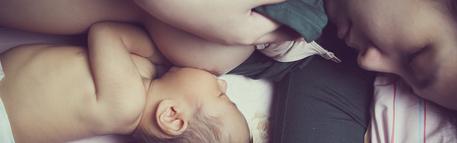 Person lifting their shirt to breastfeed and baby snuggled up against their breast and tummy