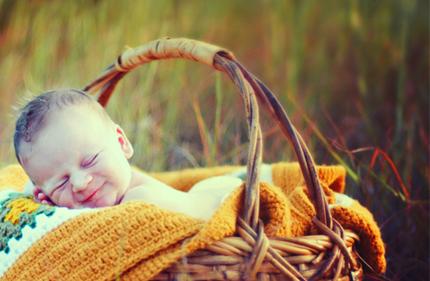 Smiley baby in a basket lined with a blanket in the middle of tall grasses