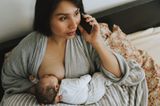 Baby laying on breastfeeding pillow with parent hunched over supporting baby's neck with one hand